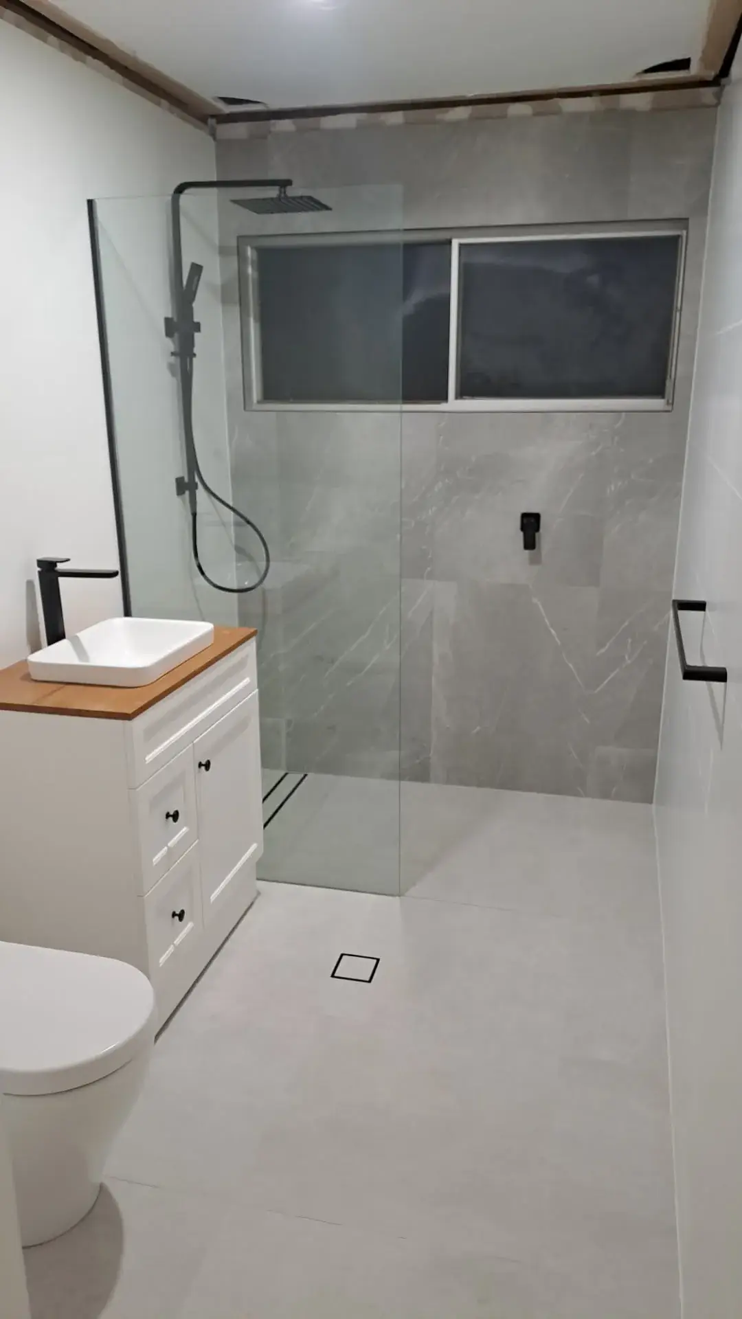 Finished Newcastle bathroom from the same doorway: walk-in shower, grey tile and black tapware