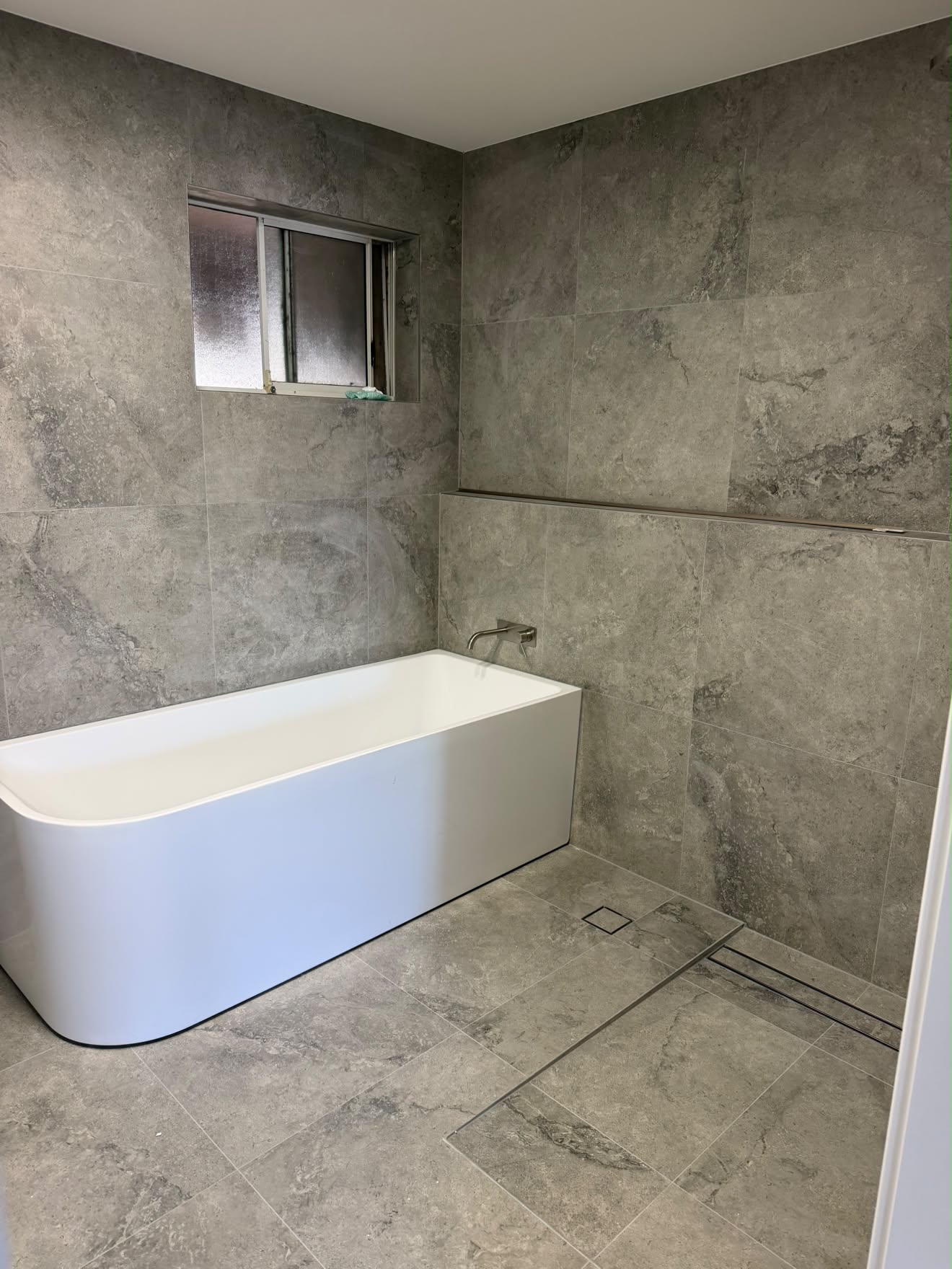 Finished bath, Lake Munmorah: back-to-wall bath on grey stone tile.