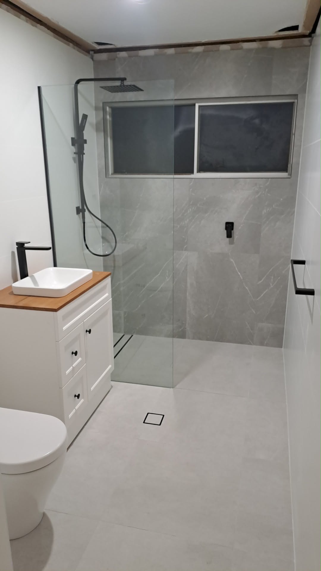 Finished Newcastle bathroom from the same doorway: walk-in shower, grey tile and black tapware
