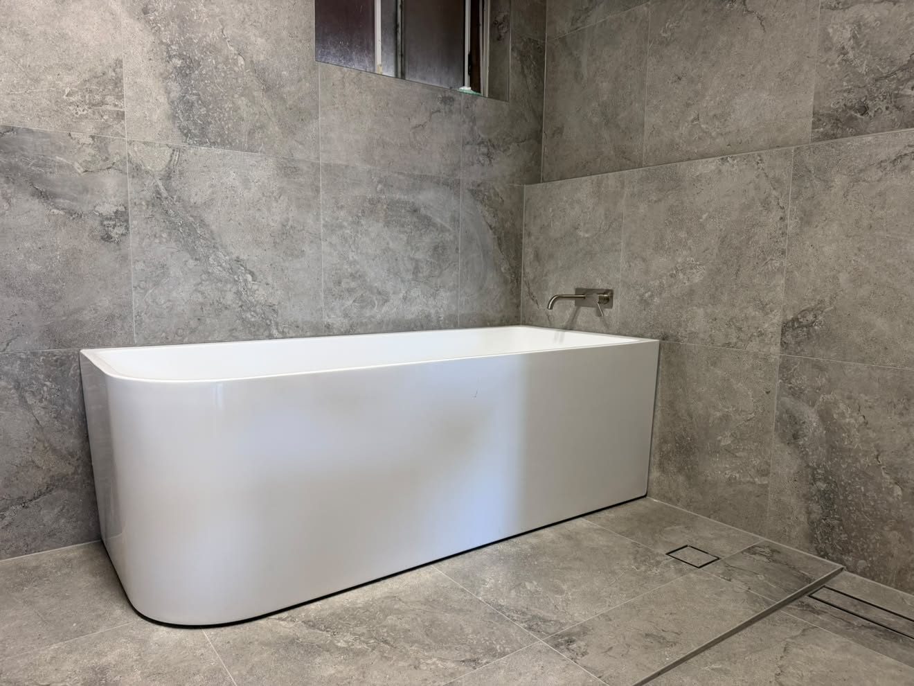 Back-to-wall bath, wall spout and a tiled-in linear floor drain.