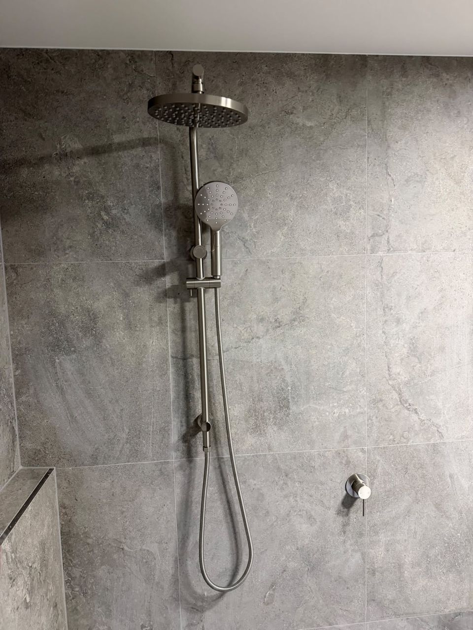 Brushed nickel rail shower and wall mixer on stone-look tile.